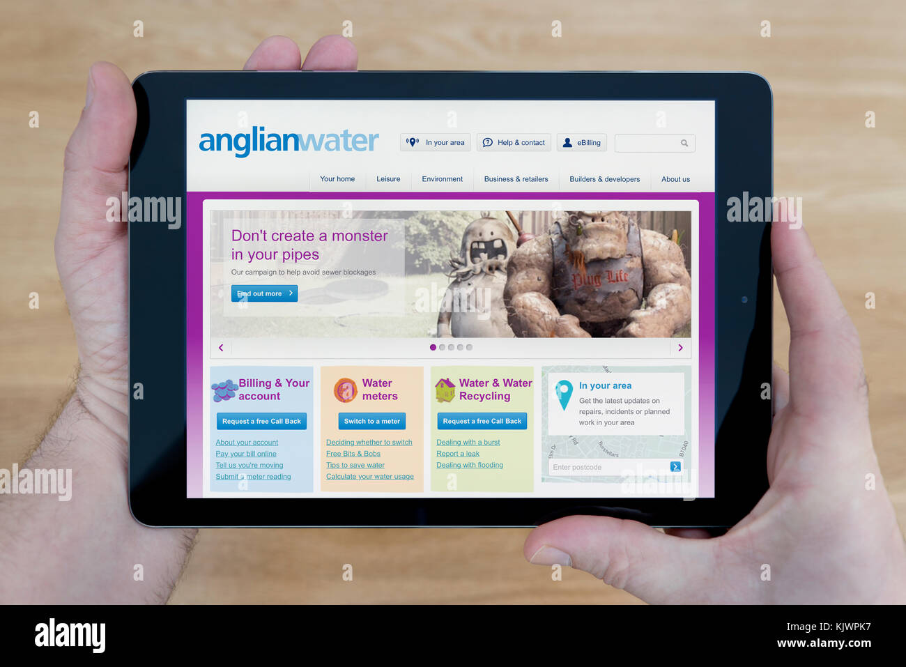 A man looks at the Anglian Water website on his iPad tablet device, shot against a wooden table top background (Editorial use only) Stock Photo