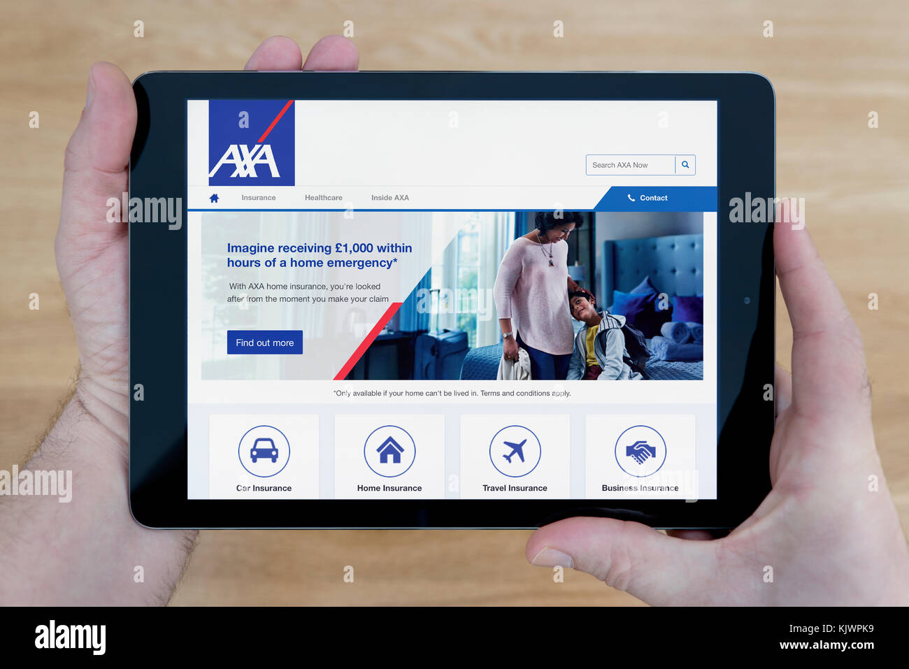 A man looks at the AXA website on his iPad tablet device, shot against a wooden table top background (Editorial use only) Stock Photo
