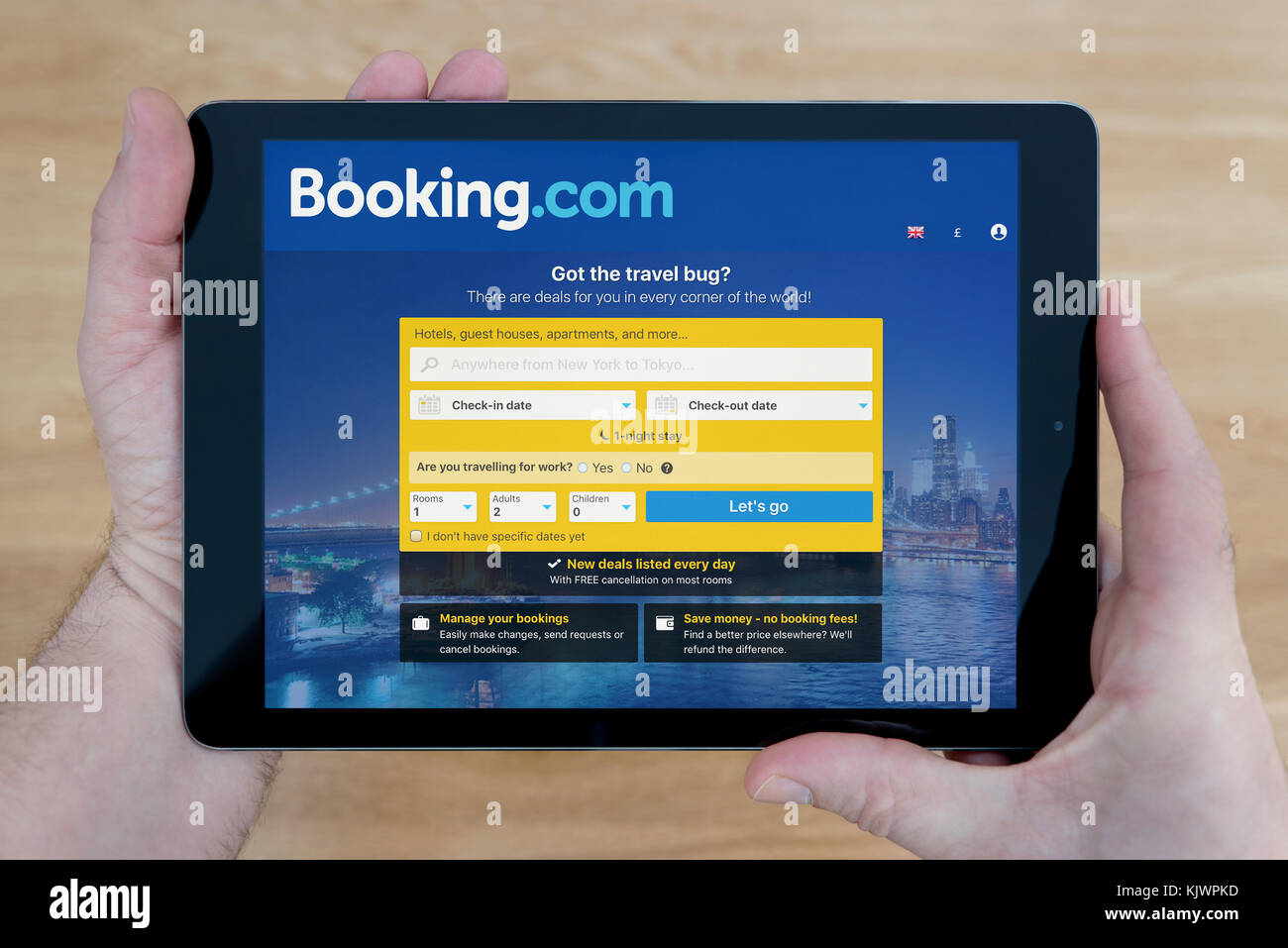 A man looks at the Booking.com website on his iPad tablet device, shot against a wooden table top background (Editorial use only) Stock Photo