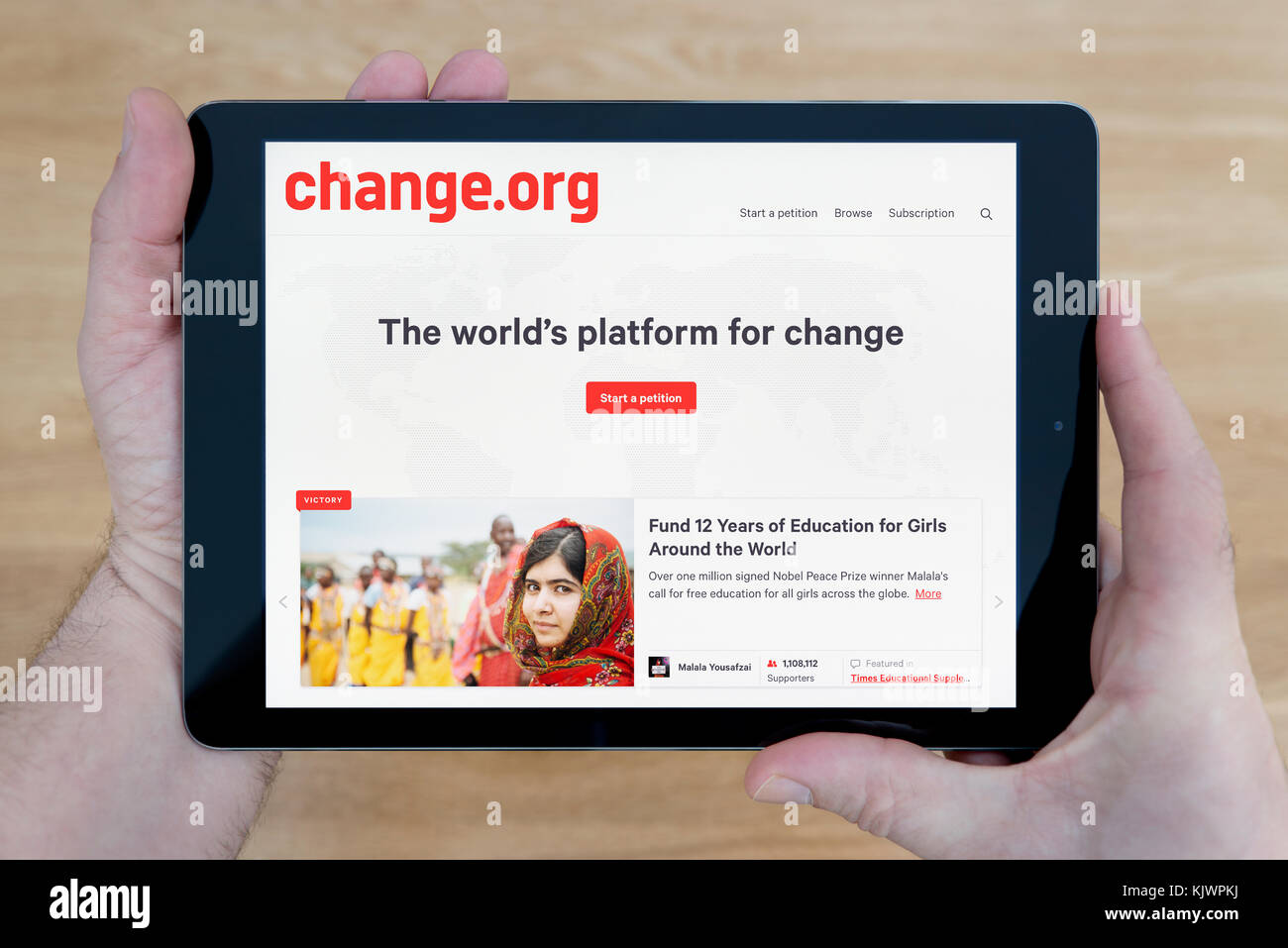 A man looks at the change.org website on his iPad tablet device, shot against a wooden table top background (Editorial use only) Stock Photo