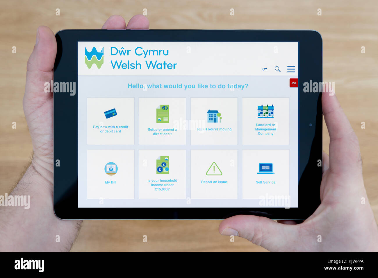 A man looks at the Dŵr Cymru Welsh Water (DCWW) website on his iPad tablet device, shot against a wooden table top background (Editorial use only) Stock Photo