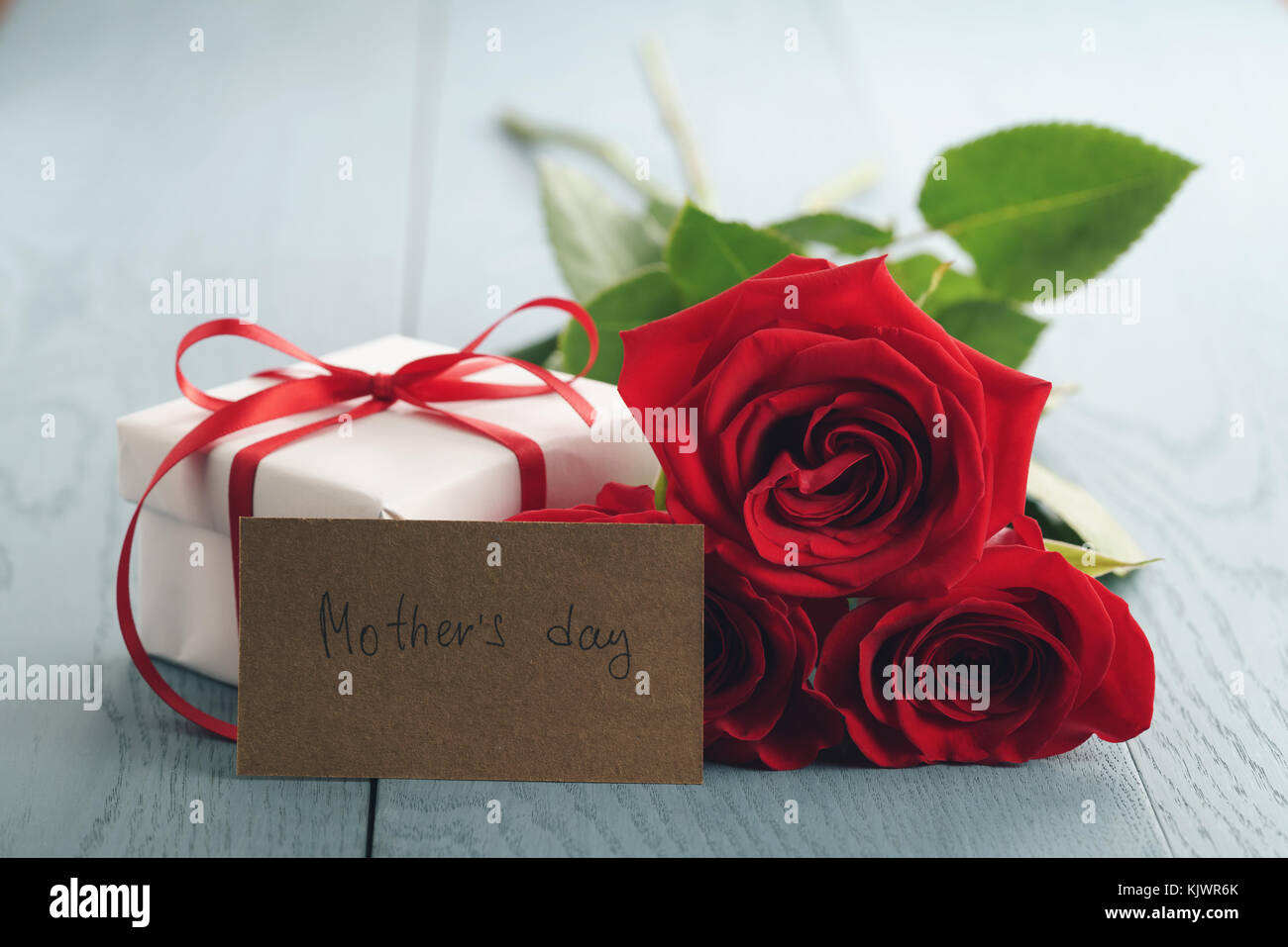 three red roses on blue wood table with gift and mothers day paper card Stock Photo