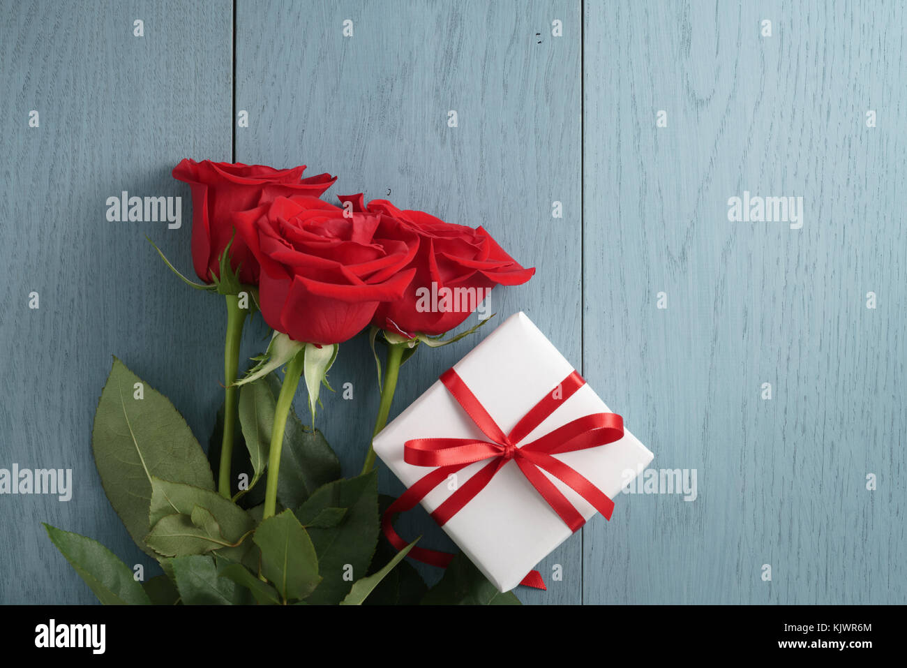 three red roses and a gift box on blue wood table with copy space Stock Photo