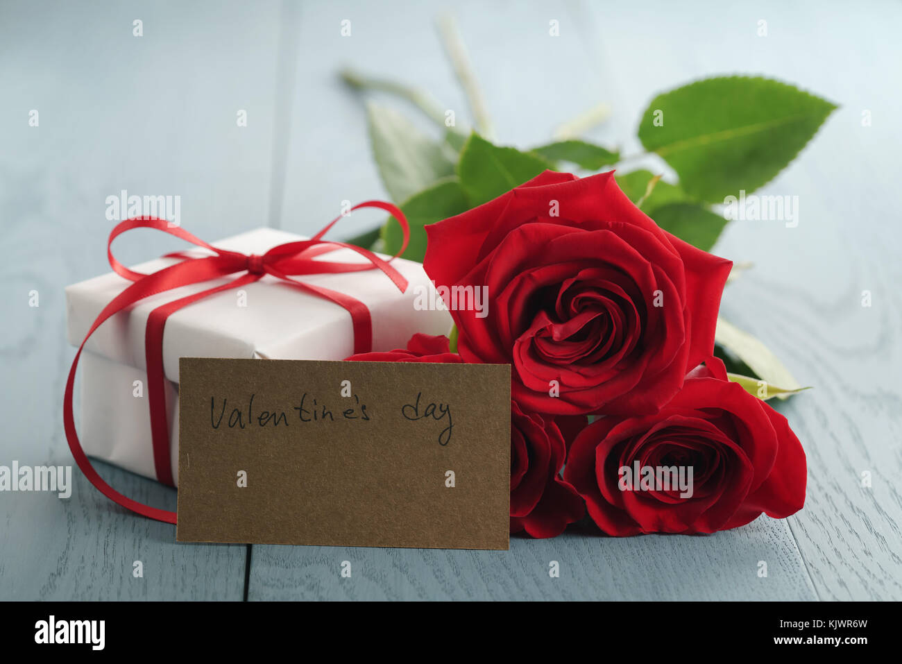 three red roses on blue wood table with gift and valentines day paper ...