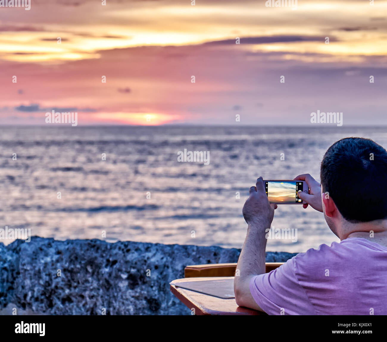 man looks through monitor of mobile phone on sunset at Cafe del Mar, Cartagena de Indias, Colombia, South America Stock Photo
