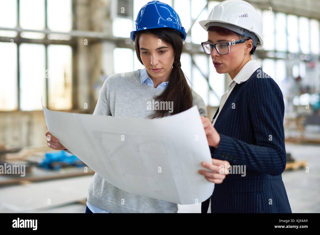 Confident beautiful businesswoman in hardhat explaining blueprint to forewoman at construction site Stock Photo