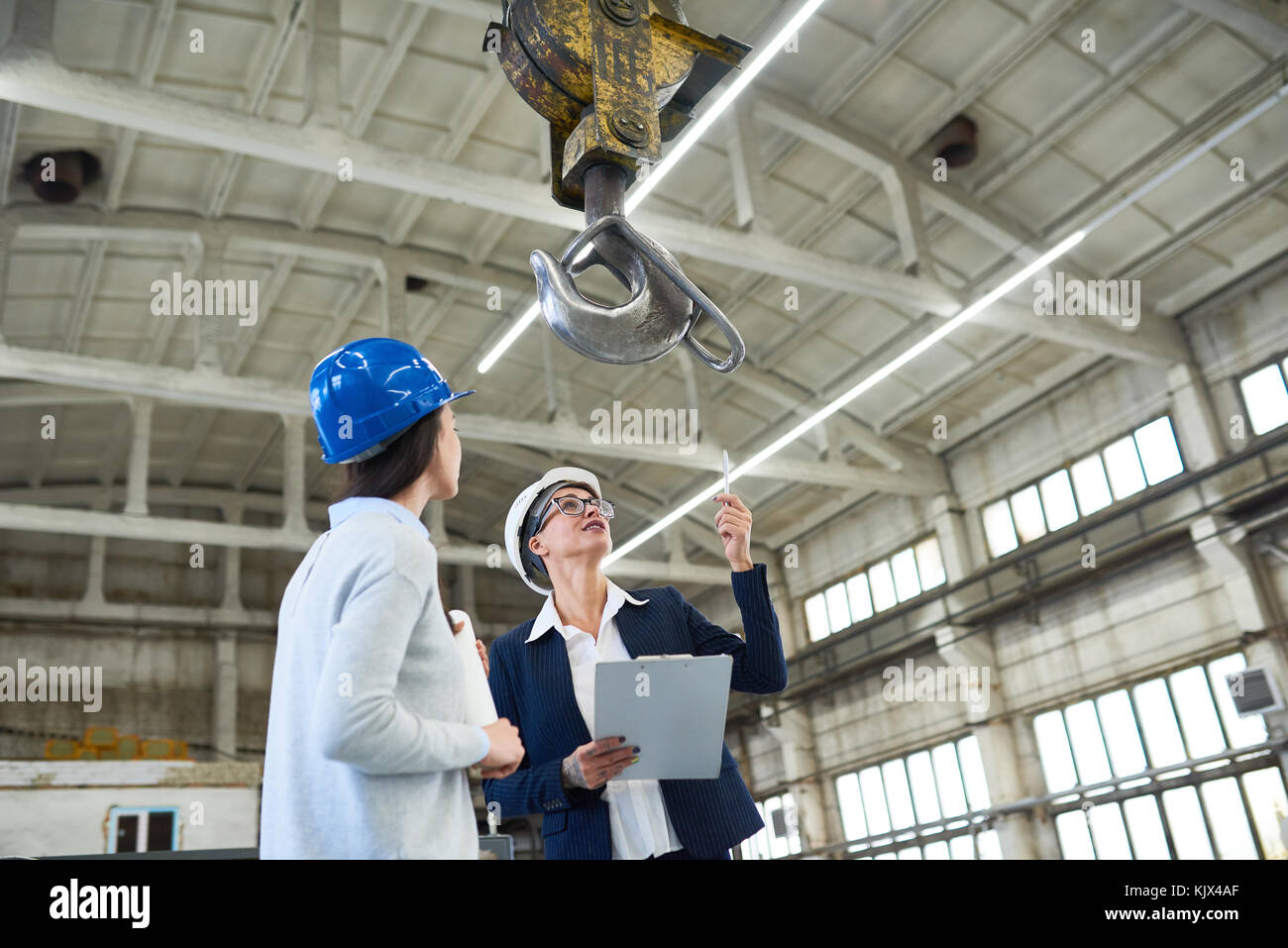 Cheerful female investor in hardhat pointing at construction crane and discussing building with forewoman at construction site Stock Photo