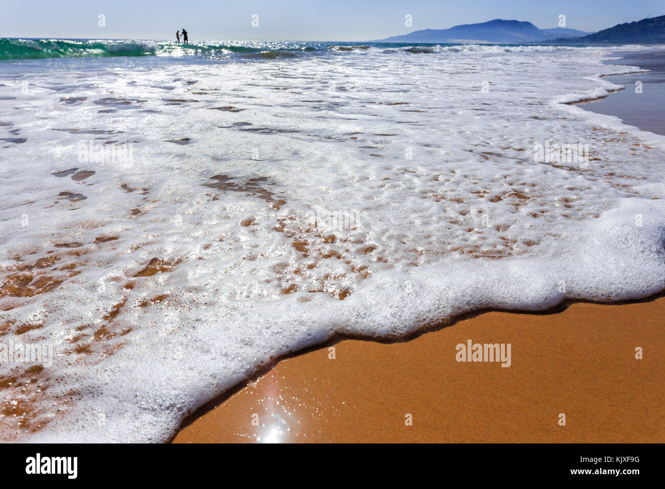 Sea wave or sea foam on the beach at sunny summer day. Two people ...