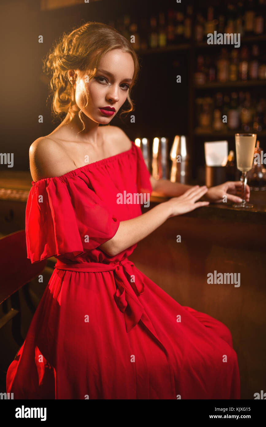 Portrait of young woman in red dress standing at the bar counter