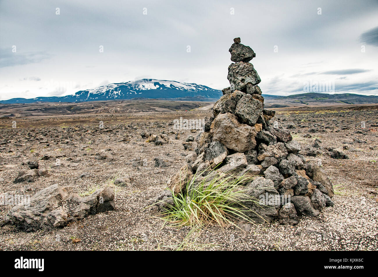 A tuft of grass grows at the foot of the solitary cairn that marks the beginning of the F225 track, at the foot of the Hekla volcano in Iceland Stock Photo