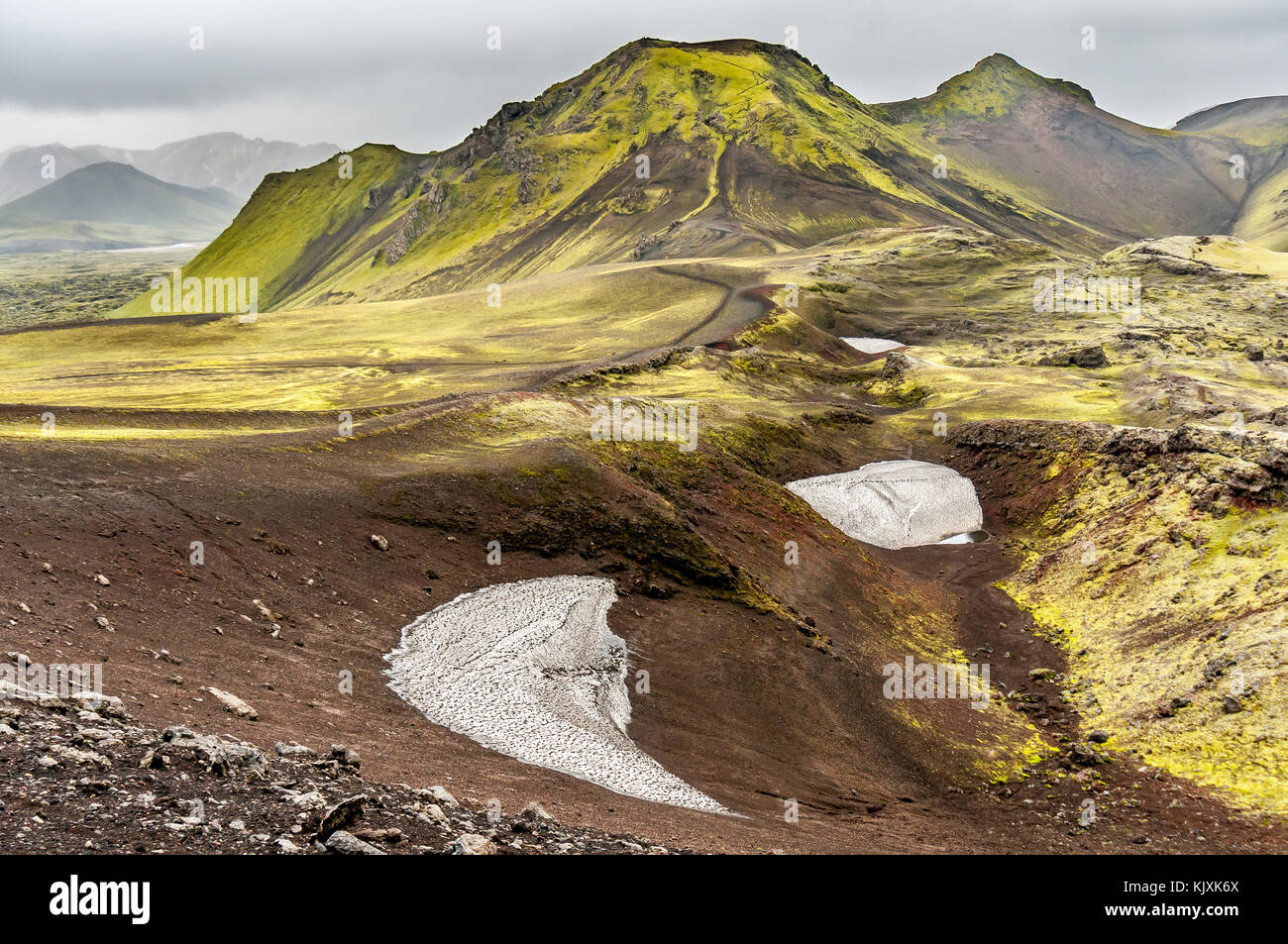 Snow Plates, Red Rock, Green Grass and Volcanic Mountain in the Landmannalaugar Region in Iceland Stock Photo
