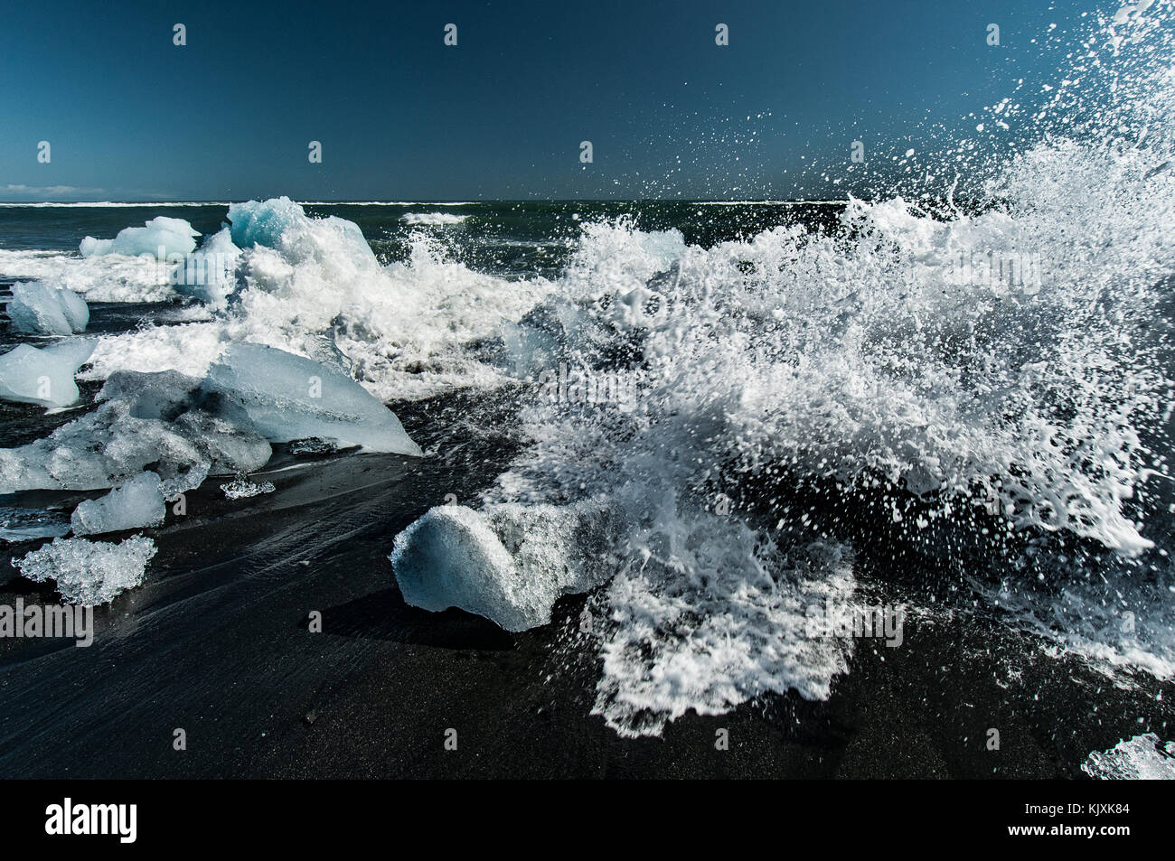 The waves of the ocean play with the Ice blocks rejected on the black volcanic beach near the Jökulsárlón in Iceland Stock Photo