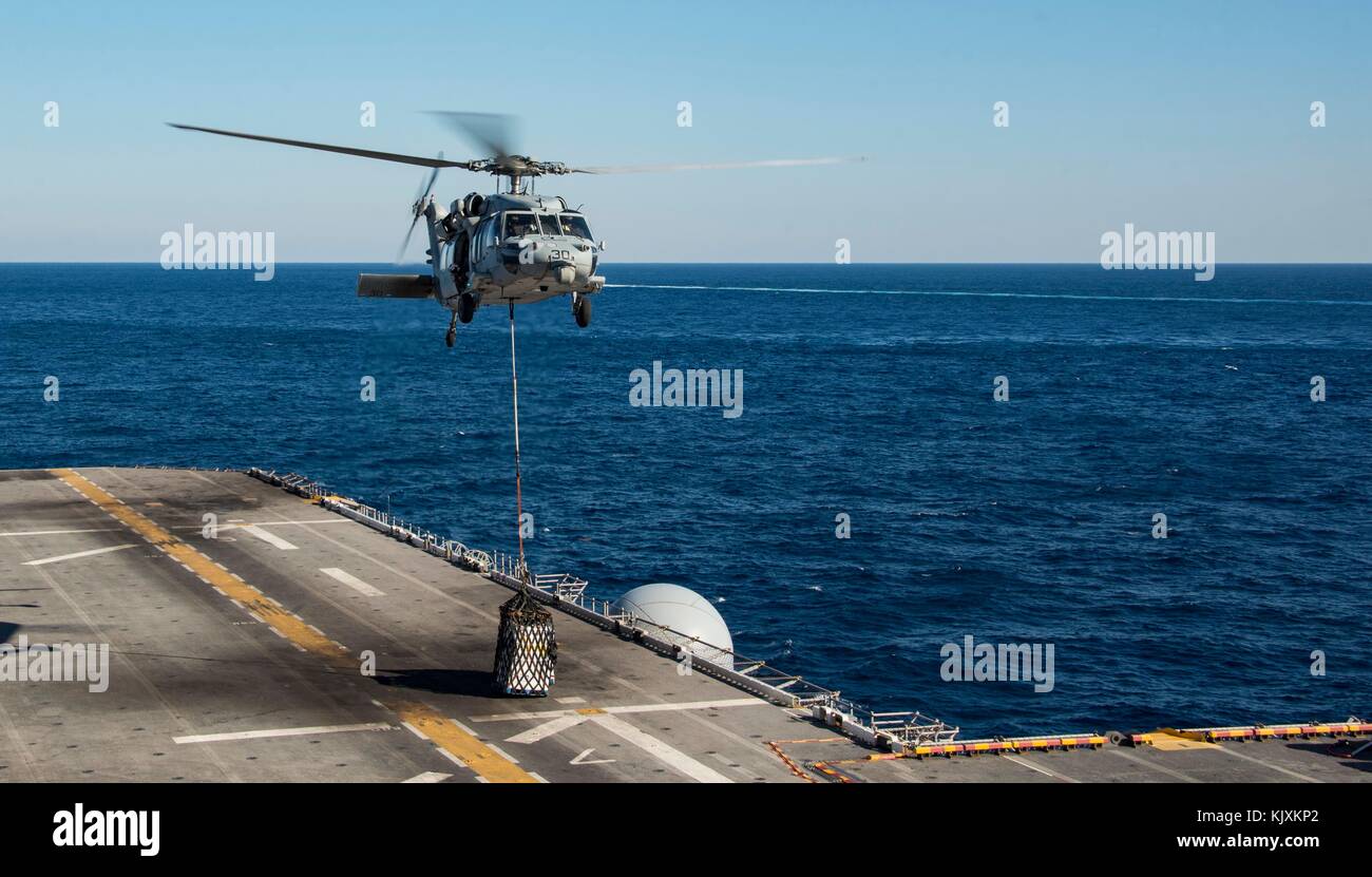An MH-60S Sea Hawk attached to Helicopter Sea Combat Squadron 28 places a pallet onto the flight deck of the amphibious Stock Photo