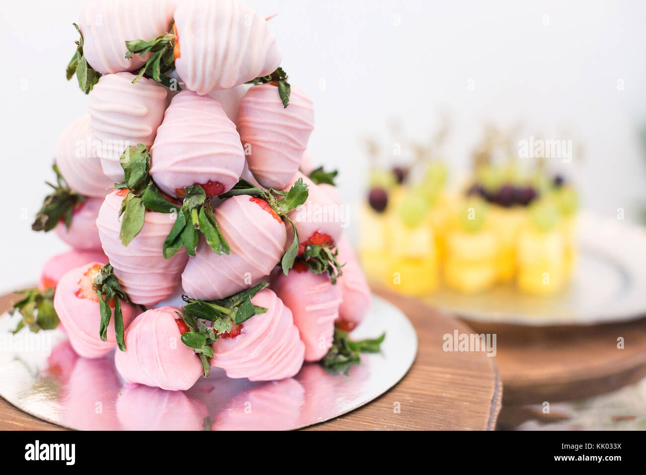 confectionary, treatment, dessert concept. close up of small pyramid on the wooden tray, it is created of strawberries that covered with light pink sweet frosting Stock Photo