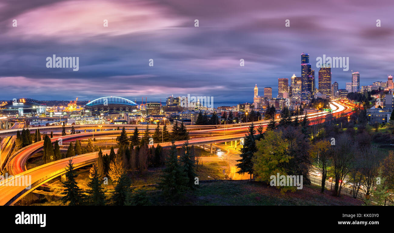 Seattle cityscape at dusk with skyscrapers, winding highways parks and sports arenas under a dramatic sky. Stock Photo