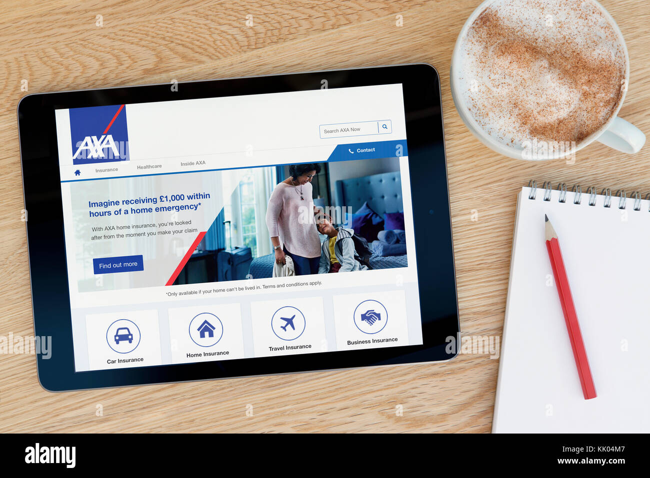A man looks at the AXA website on his iPad tablet device, shot against a wooden table top background (Editorial use only) Stock Photo