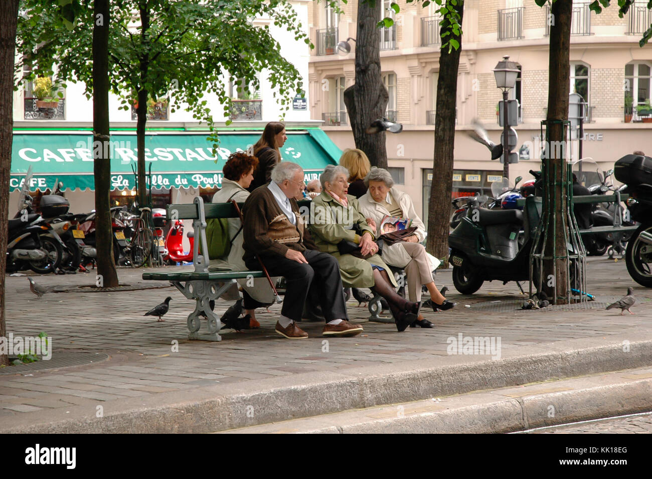 Elderly Parisians sitting on the bench on a Paris street talking and watching people and traffic passing by. Stock Photo