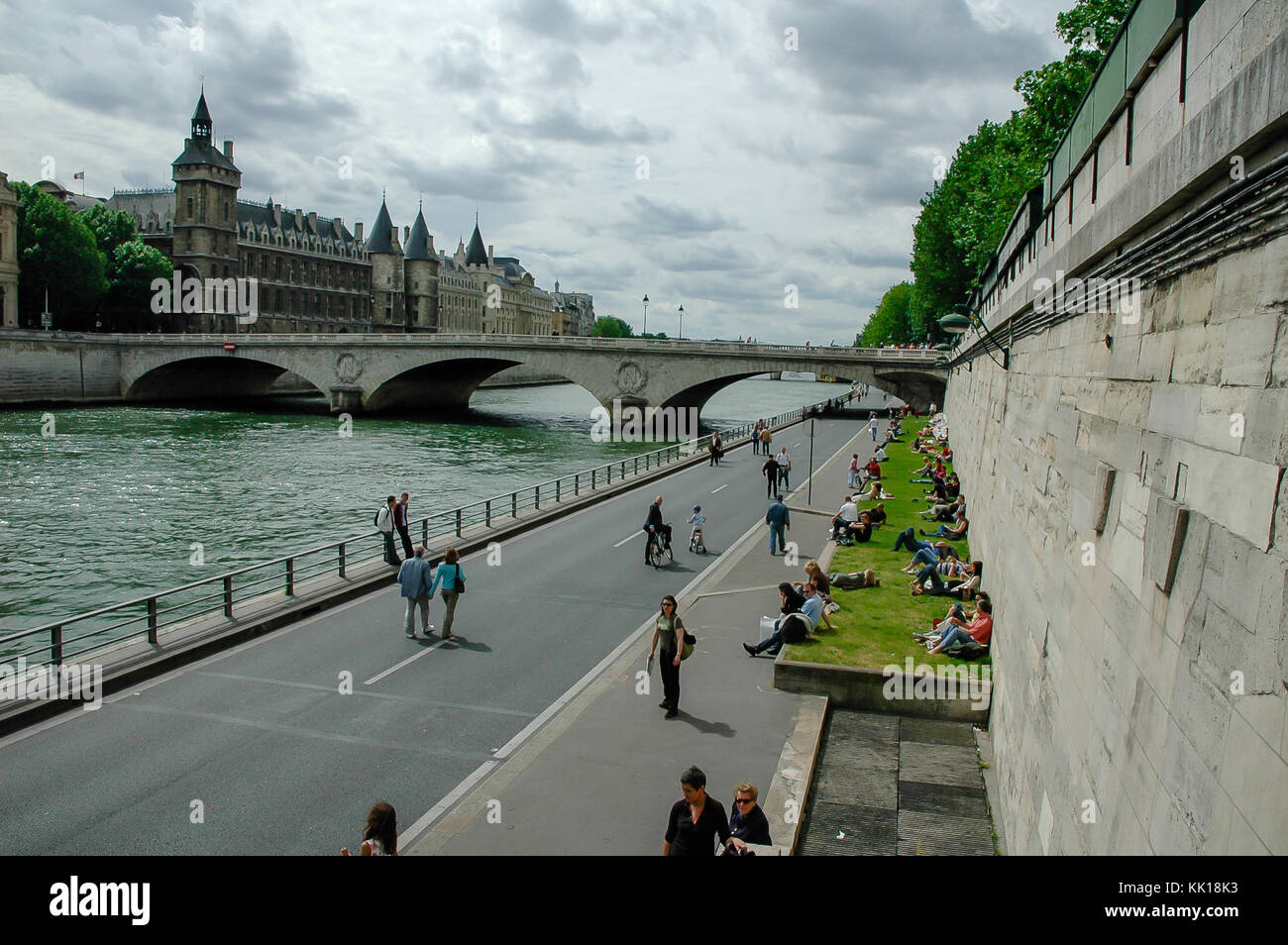 Tourists relaxing on the banks of river Seine with view on The Pont au Change bridge and the Conciergerie Fortress in the background in Paris, France Stock Photo