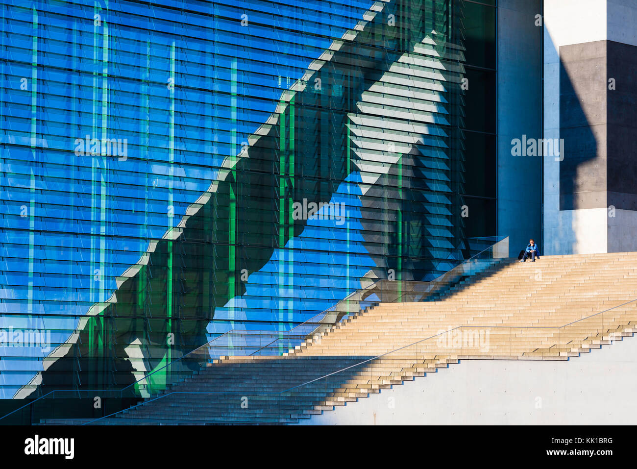 Mitte Berlin architecture, a man sits alone on a staircase alongside the huge glass facade of the Maria-Elisabeth-Luders Haus in Berlin, Germany. Stock Photo