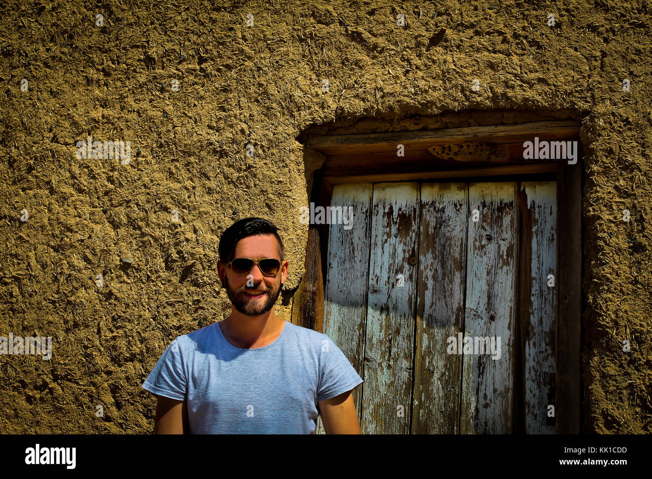 Smiling Caucasian man with sunglasses standing in front of door of mud house Stock Photo