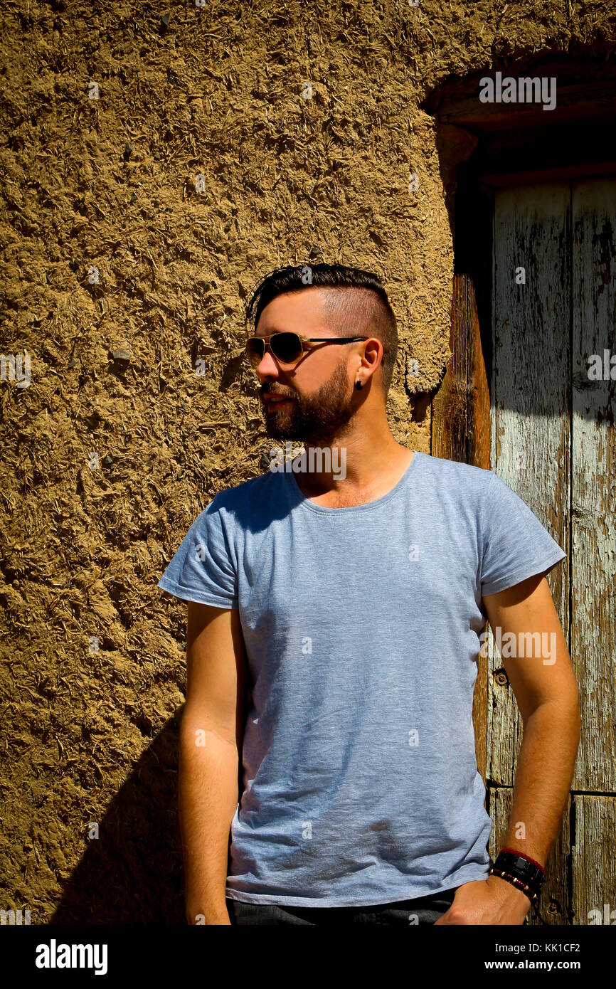 Caucasian man with sunglasses looking to the side standing in front of door of mud house Stock Photo