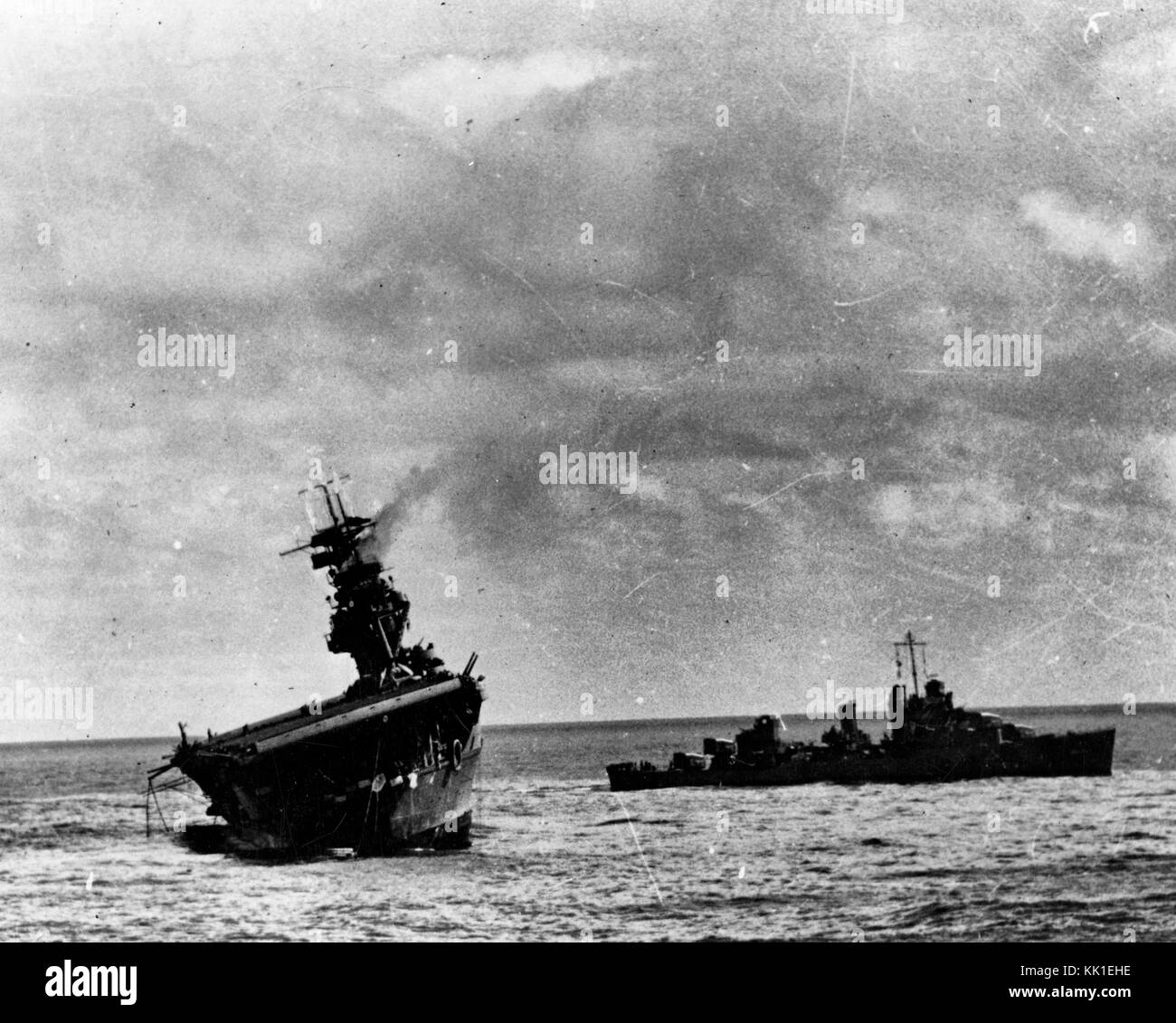 USS Yorktown (CV-5) being abandoned by her crew after she was hit by two Japanese Type 91 aerial torpedoes, 4 June 1942. USS Balch (DD-363) is standing by at right. Note oil slick surrounding the damaged carrier, and inflatable life raft being deployed off her stern. Stock Photo