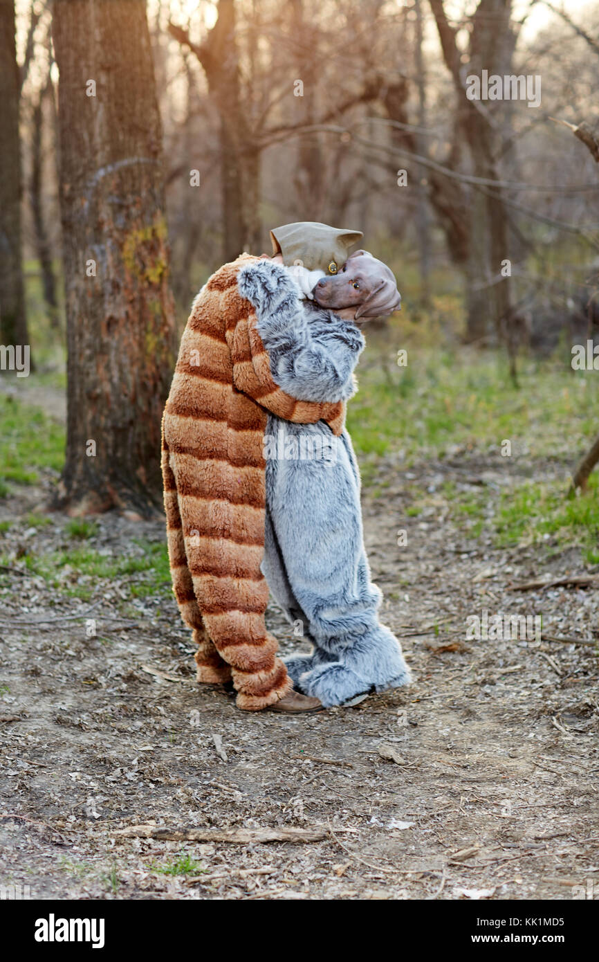 Funny couple in love hugging while wearing carnival cat and dog costumes outdoors in the forest Stock Photo