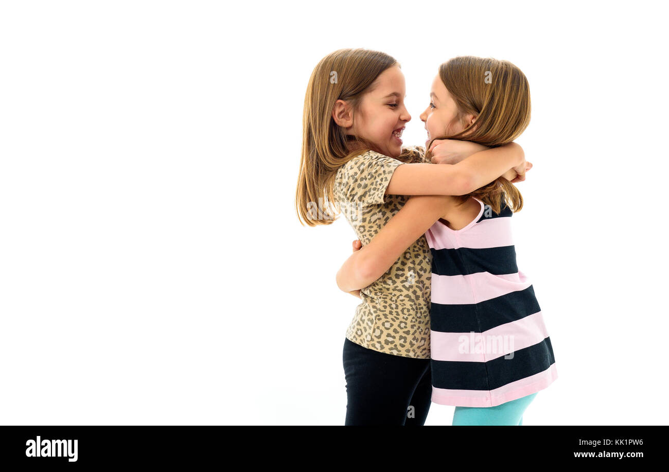 Identical twin girls are looking at each other and smiling. Concept of family and sisterly love. Profile side view of sisters playing, hugging, smilin Stock Photo