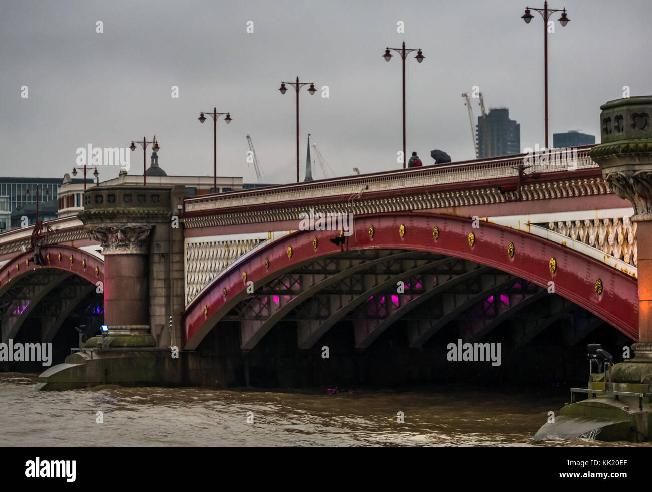 View of people walking on Blackfriars Bridge over River Thames, with ornate old fashioned lamp posts, London, England, UK, on grey rainy day Stock Photo