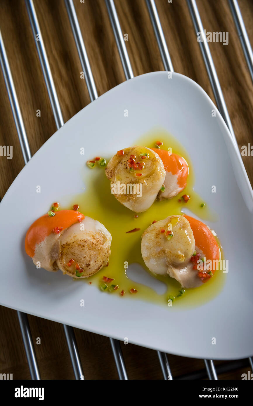 Three cooked king scallops including coral ready to serve on triangular white plate. Portrait vertical format. Stock Photo