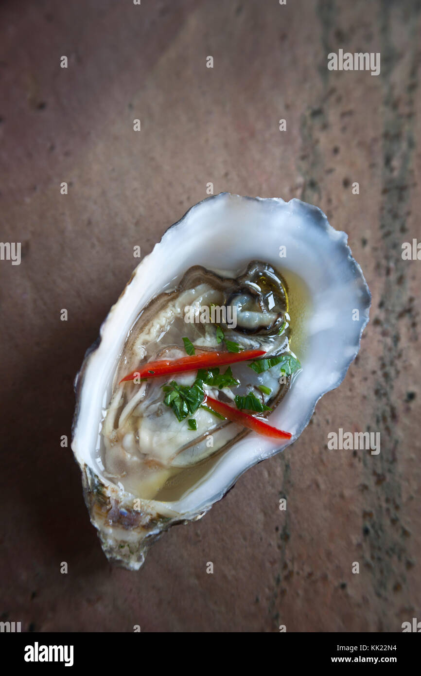 Fresh oyster in half shell with red chilli and herbs on stone base. Portrait vertical format. Stock Photo
