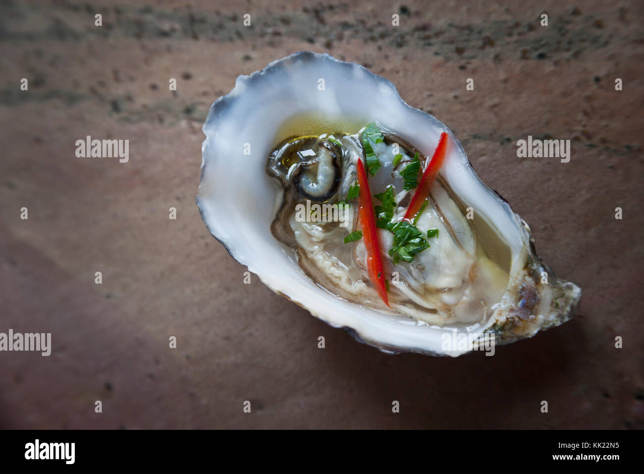 Fresh oyster in half shell with red chilli and herbs on stone base Stock Photo