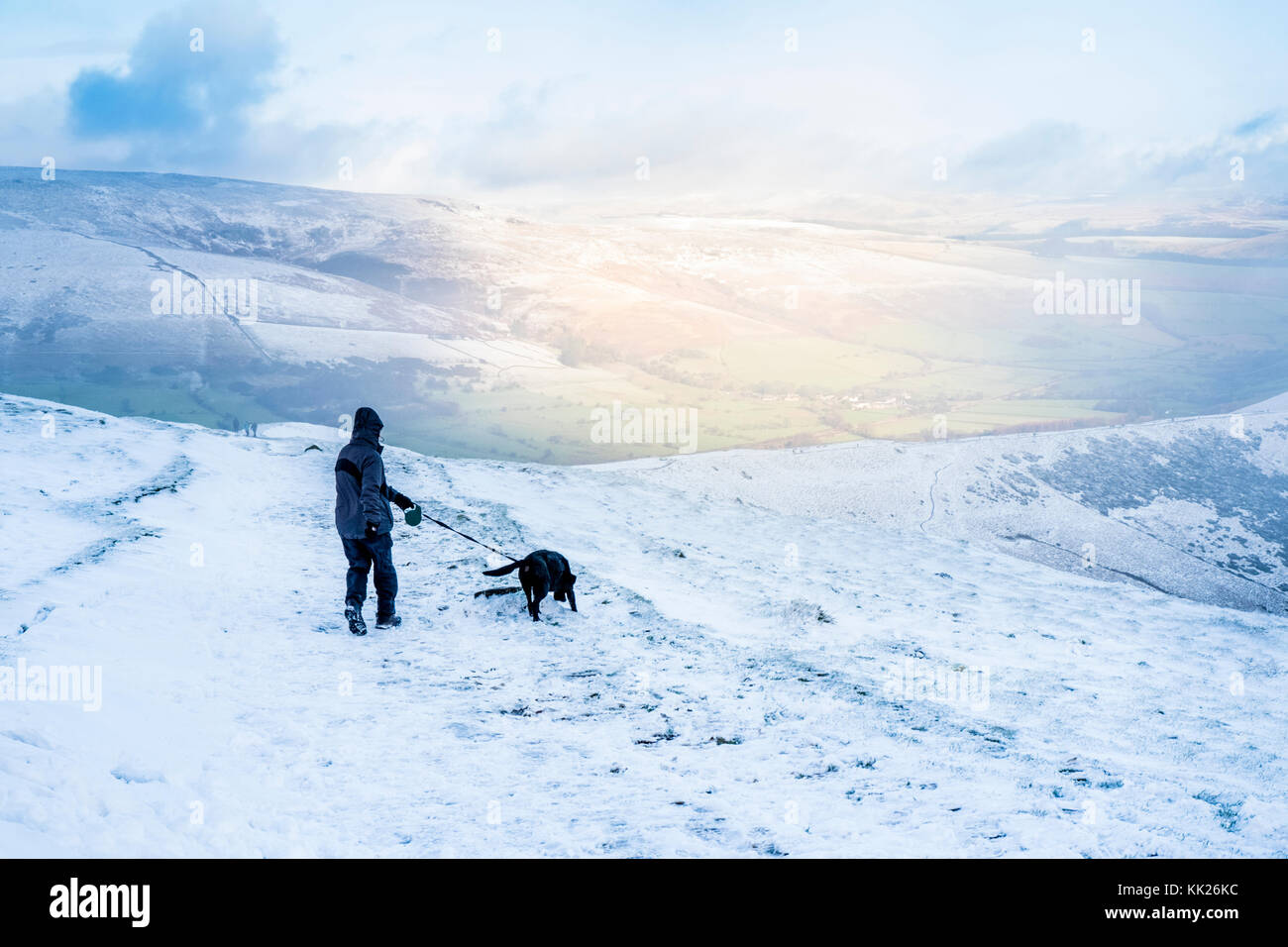 Dog walking in the snow. Hiker with dog hiking with sunlight shining on a hill across the valley. Great Ridge, Derbyshire, Peak District, England, UK Stock Photo