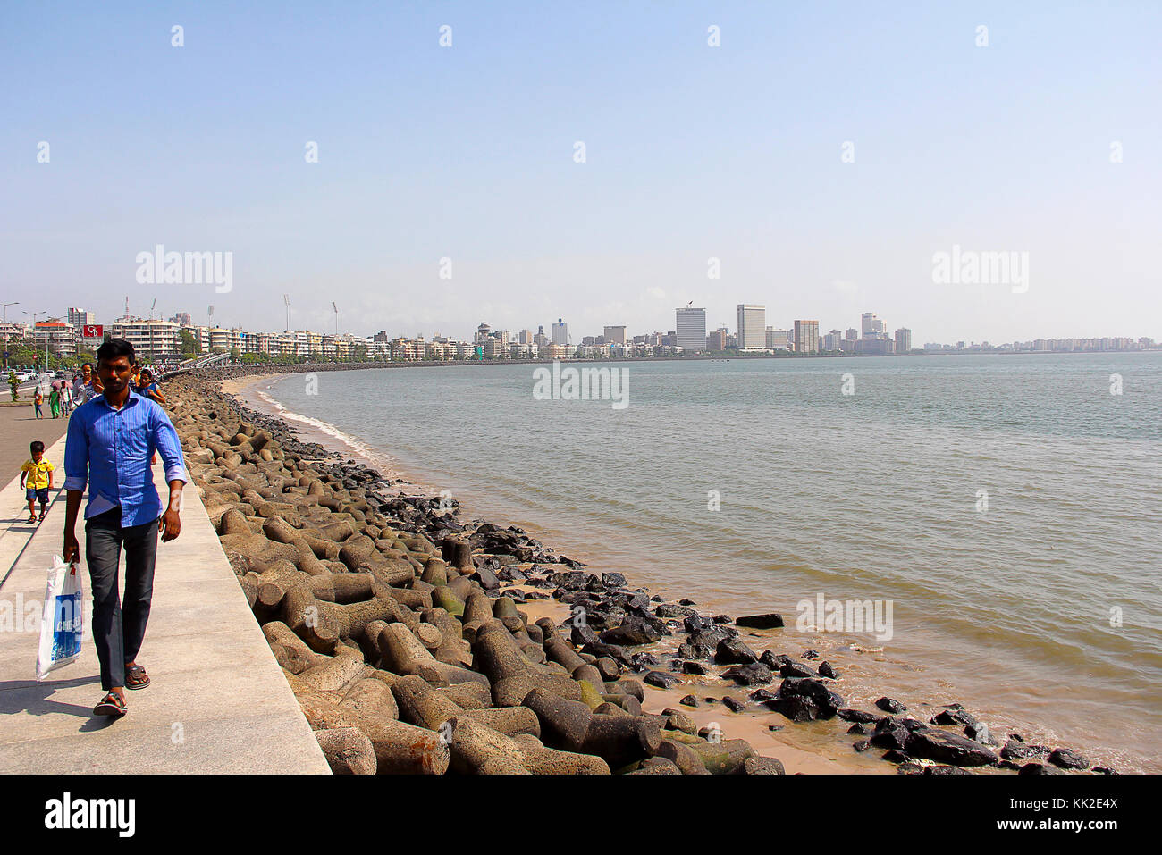 Man and people walking along side marine drive, long shot with sea and buildings, Mumbai Stock Photo