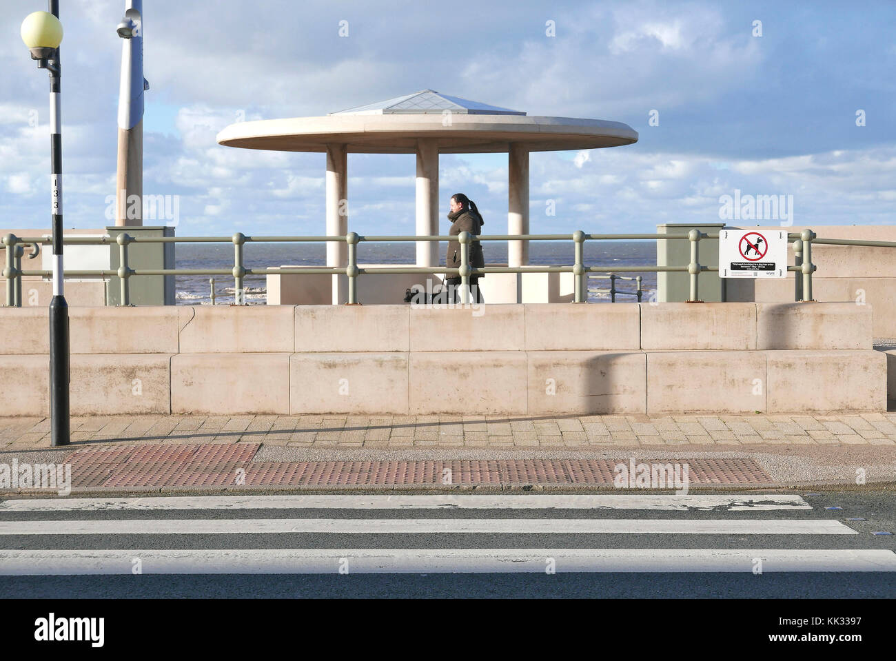 Women walking dog past concrete shelter on Cleveleys seafront in front of pedestrian crossing Stock Photo