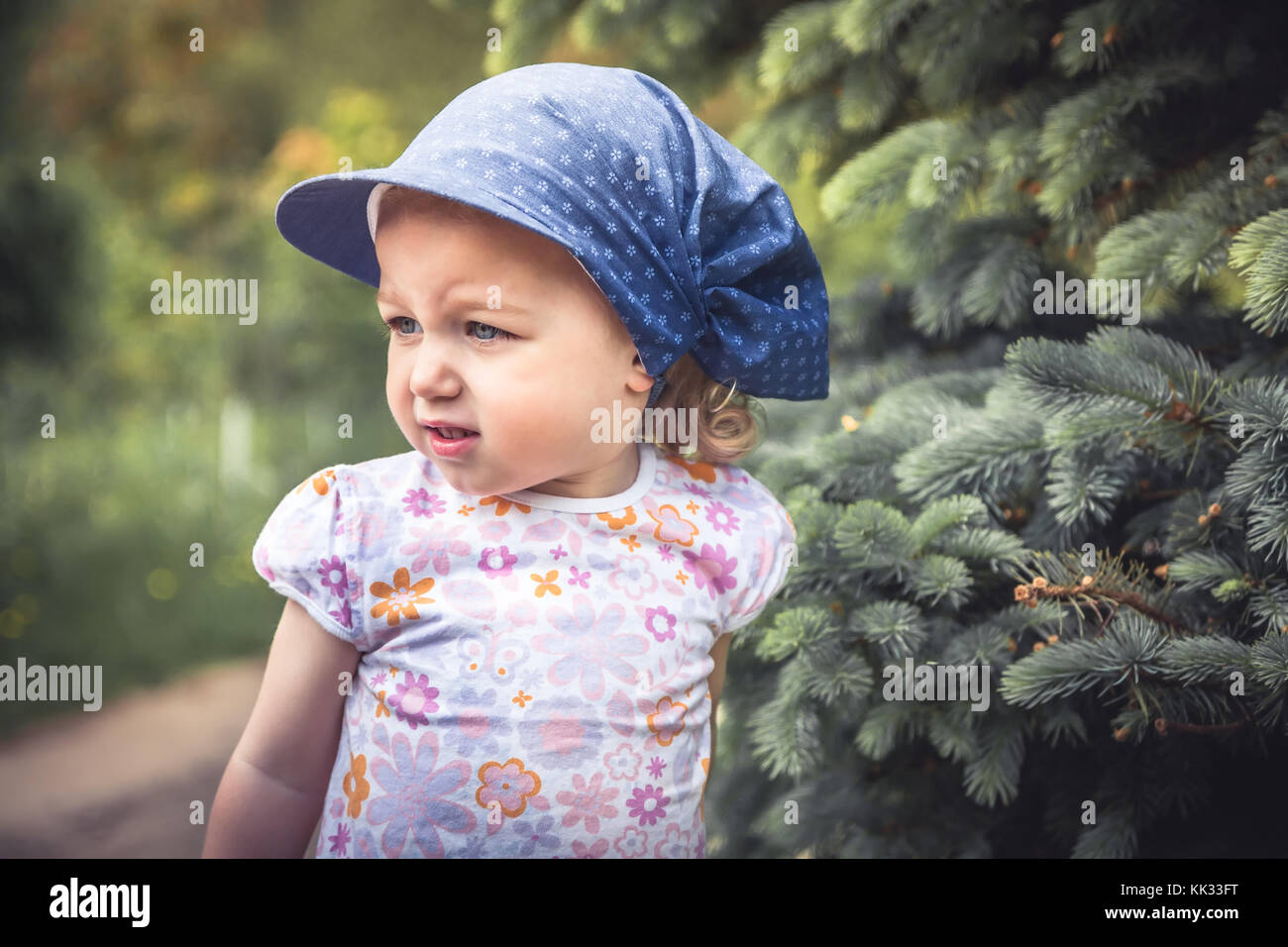 Mischievous frouned child girl portrait among fir trees on blurred background Stock Photo