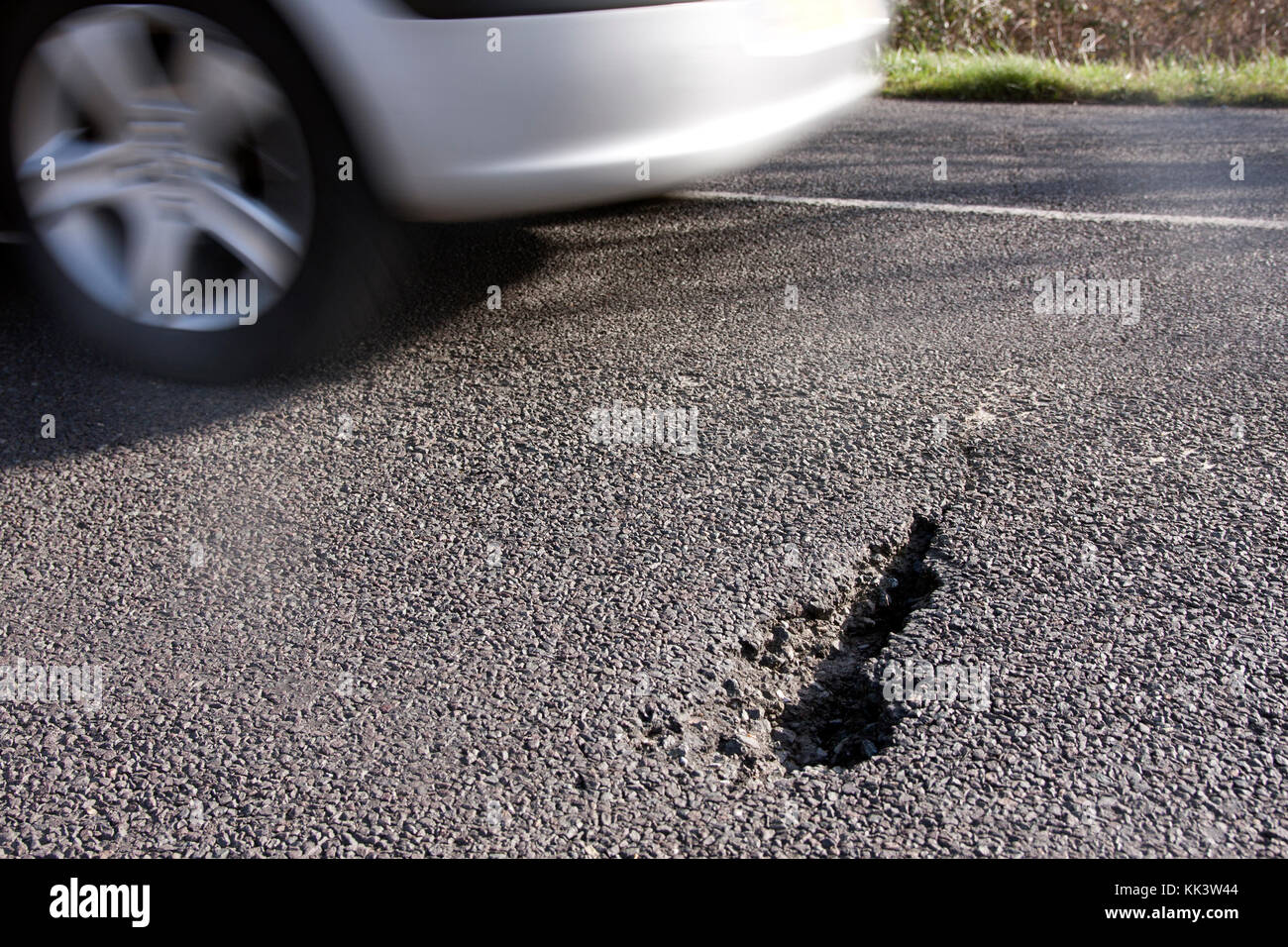 car driving past pothole in road, Sussex, England Stock Photo