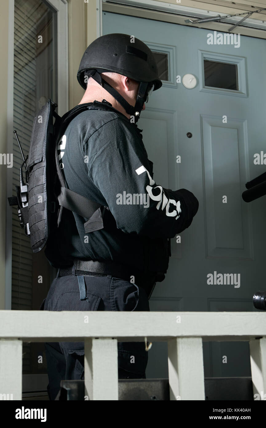 Side view of a policeman wearing helmet and uniform during a special and dangerous mission in front of the door of a suspect Stock Photo