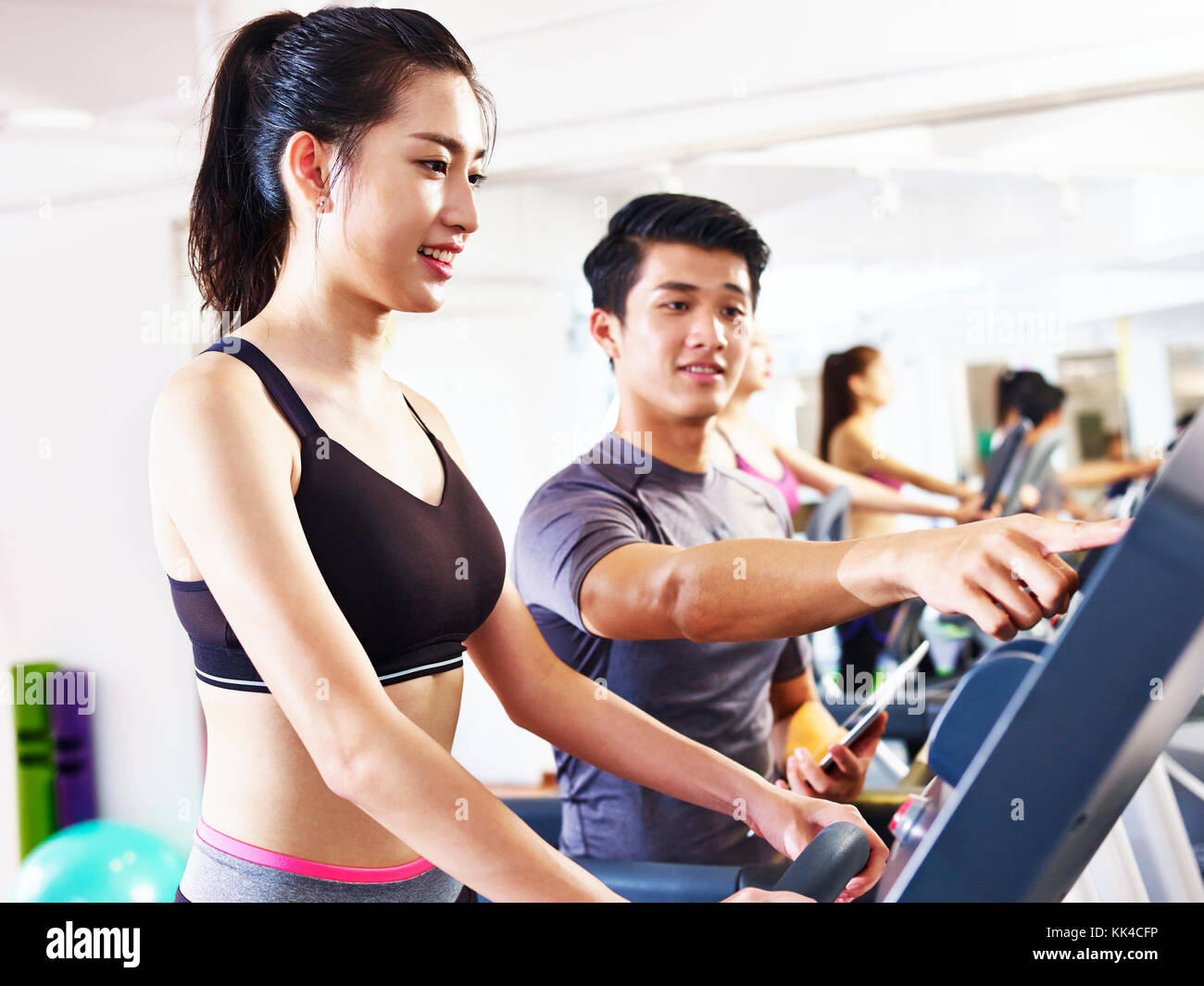 young asian woman running on treadmill coached by young male trainer. Stock Photo