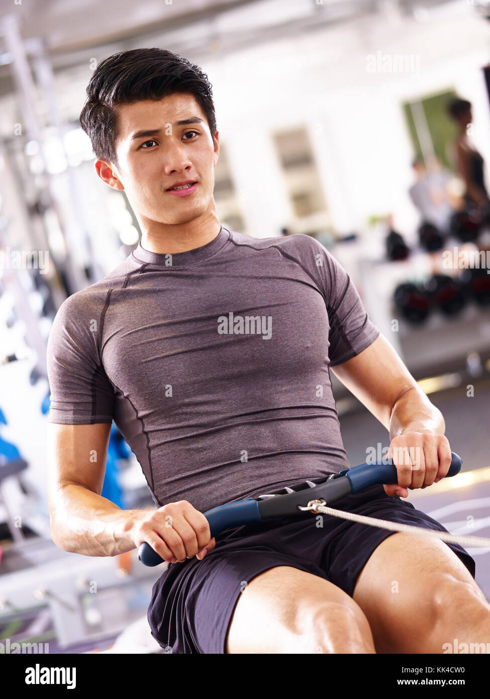 young asian adult man working out in gym using rowing machine. Stock Photo