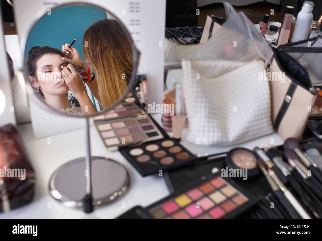 professional makeup artist doing makeup for Make up artist work in beauty salon. Reflection in the mirror as visagist applying makeup. Backstage Stock Photo -