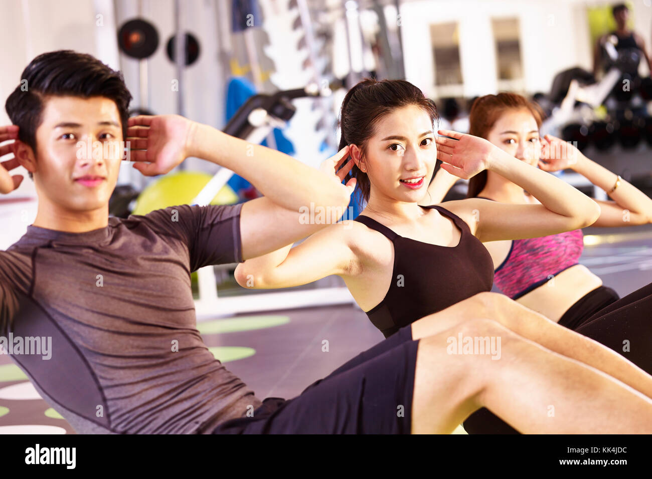 three young asian adults, male and female, doing sit-ups on the floor in gym. Stock Photo