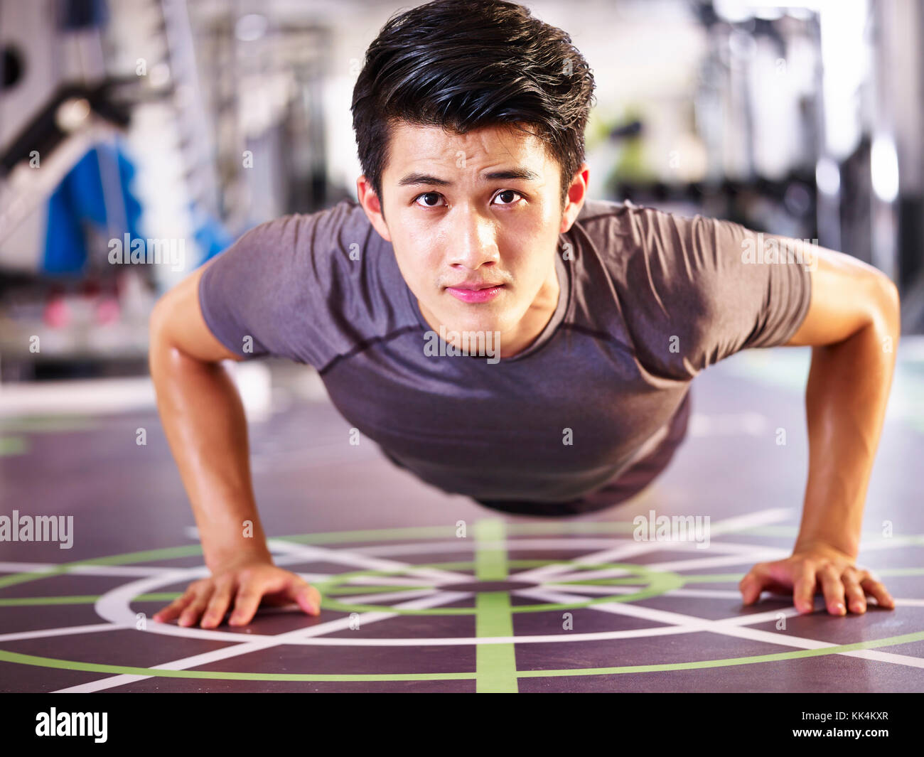 young asian adult man exercising in gym doing pushups, frontal view. Stock Photo