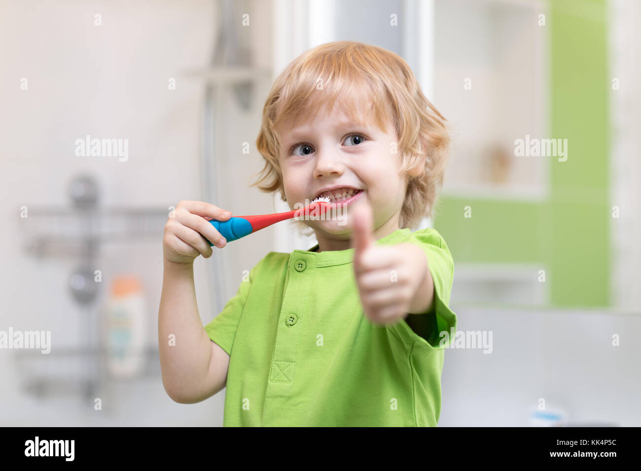 Little boy brushing his teeth in the bathroom. Smiling child holding toothbrush and showing thumbs up. Stock Photo