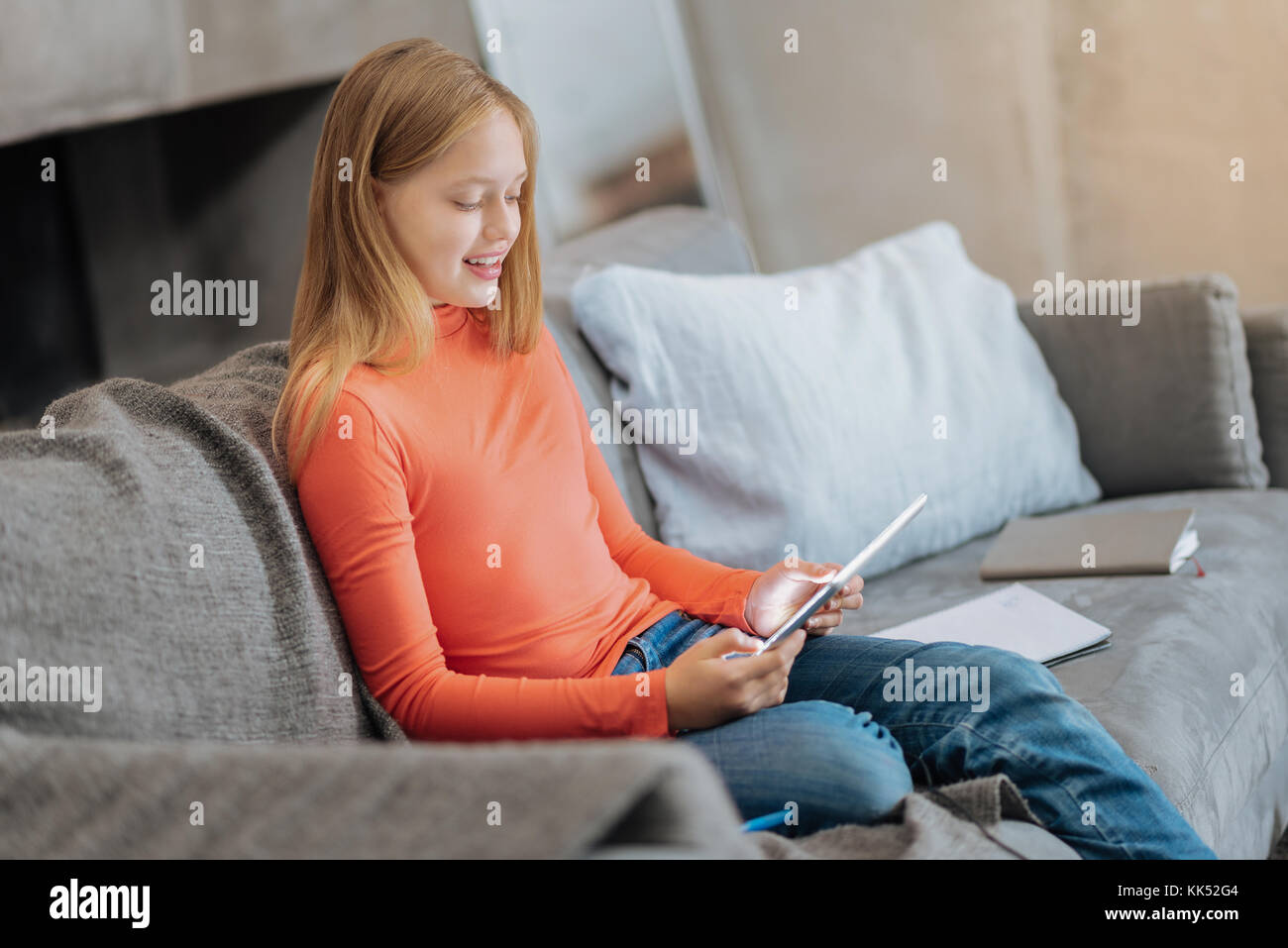 At home. Positive nice cheerful girl sitting on the sofa and holding a ...