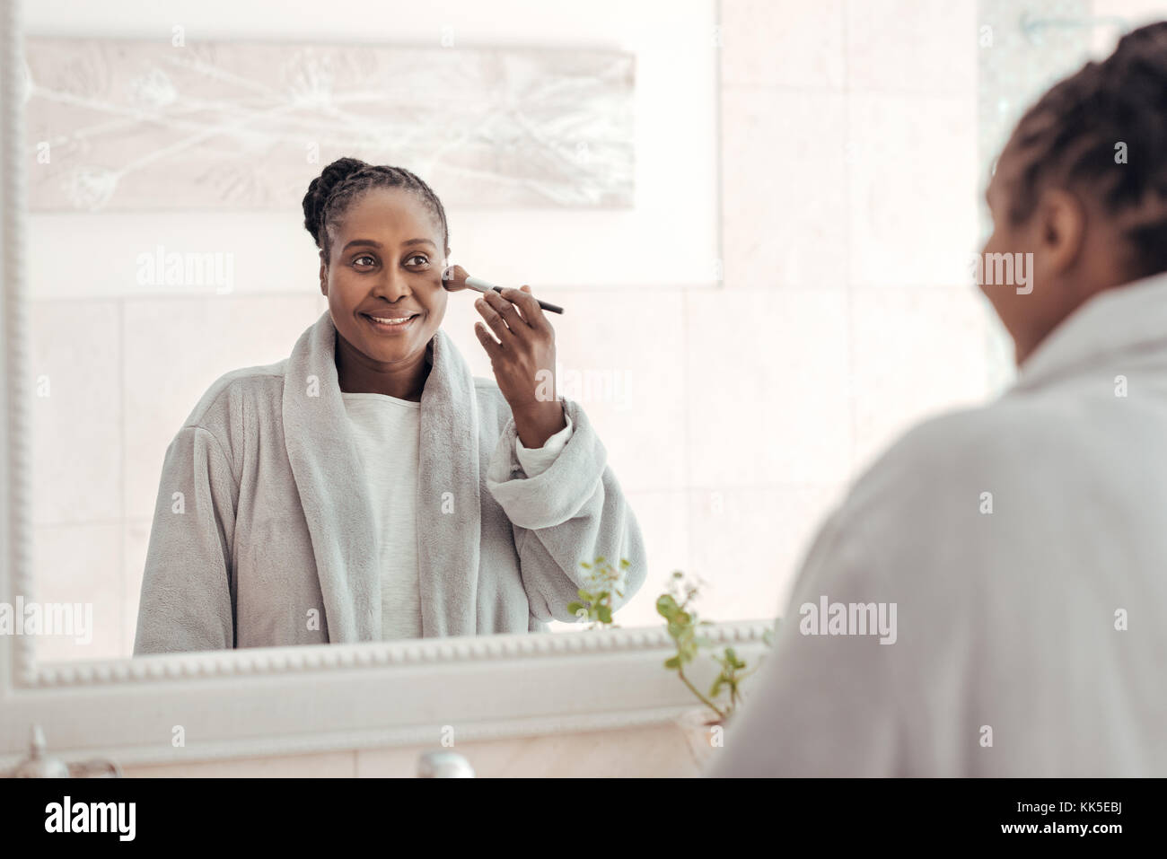 African woman applying foundation to her cheek in the bathroom Stock Photo