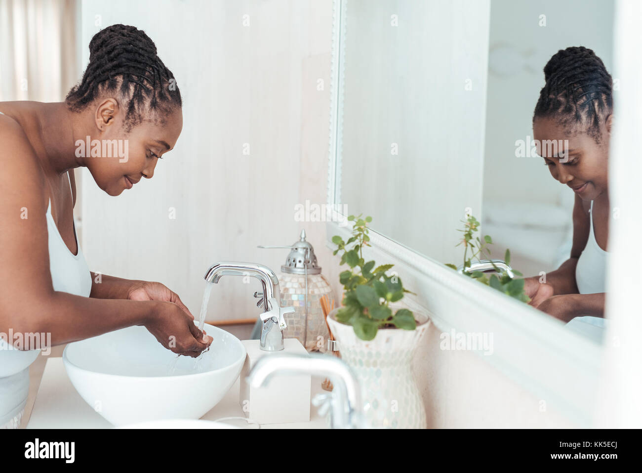 Young African woman washing her face in the bathroom sink Stock Photo