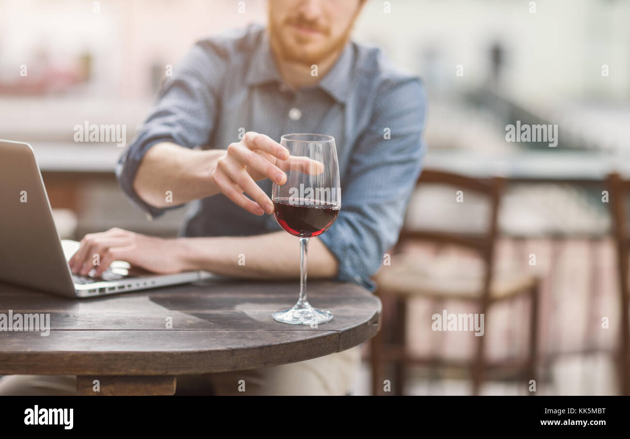 Young man sitting at outdoor bar table having a glass of red wine and ...