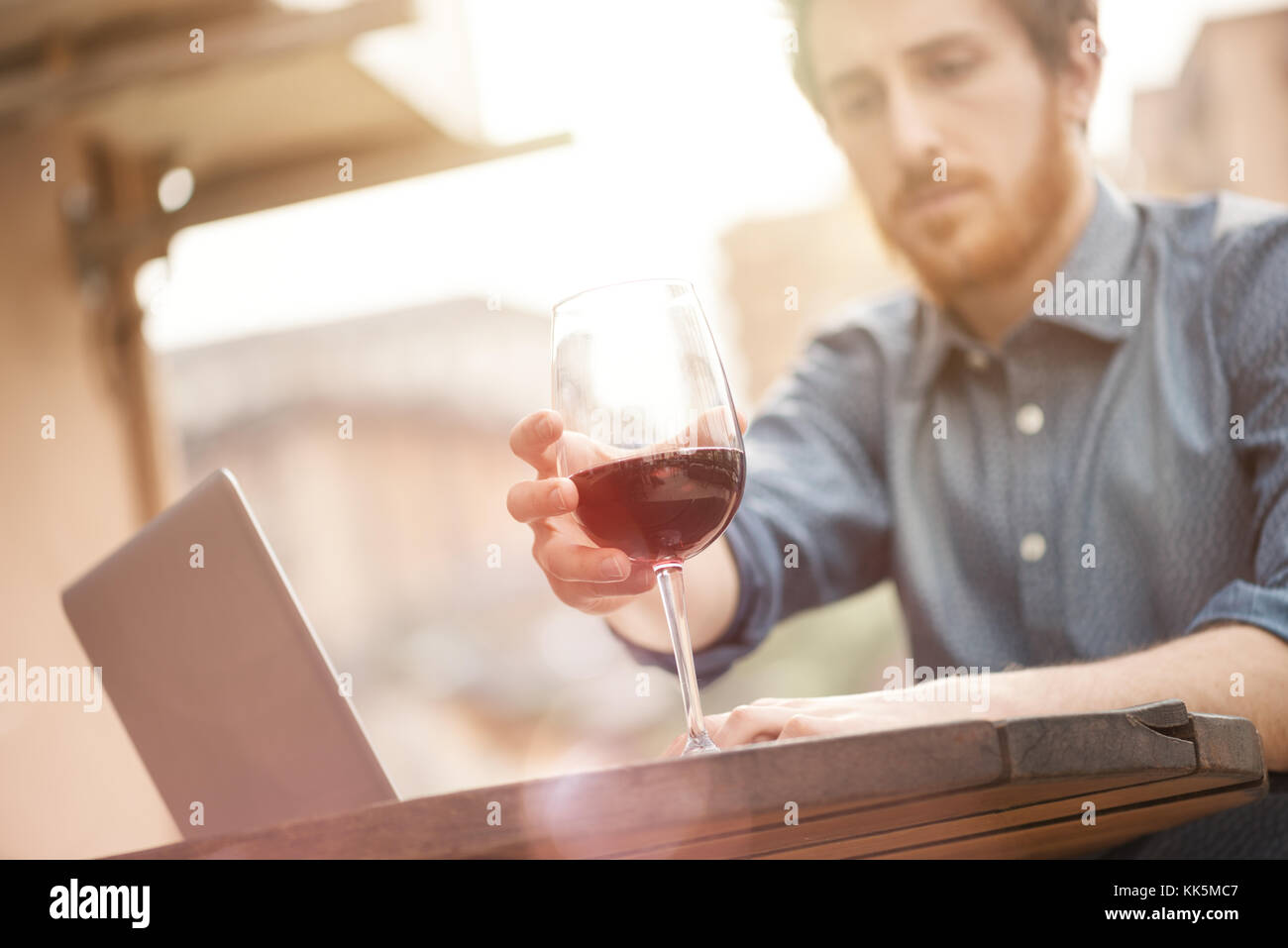 Young man sitting at outdoor bar table having a glass of red wine and ...