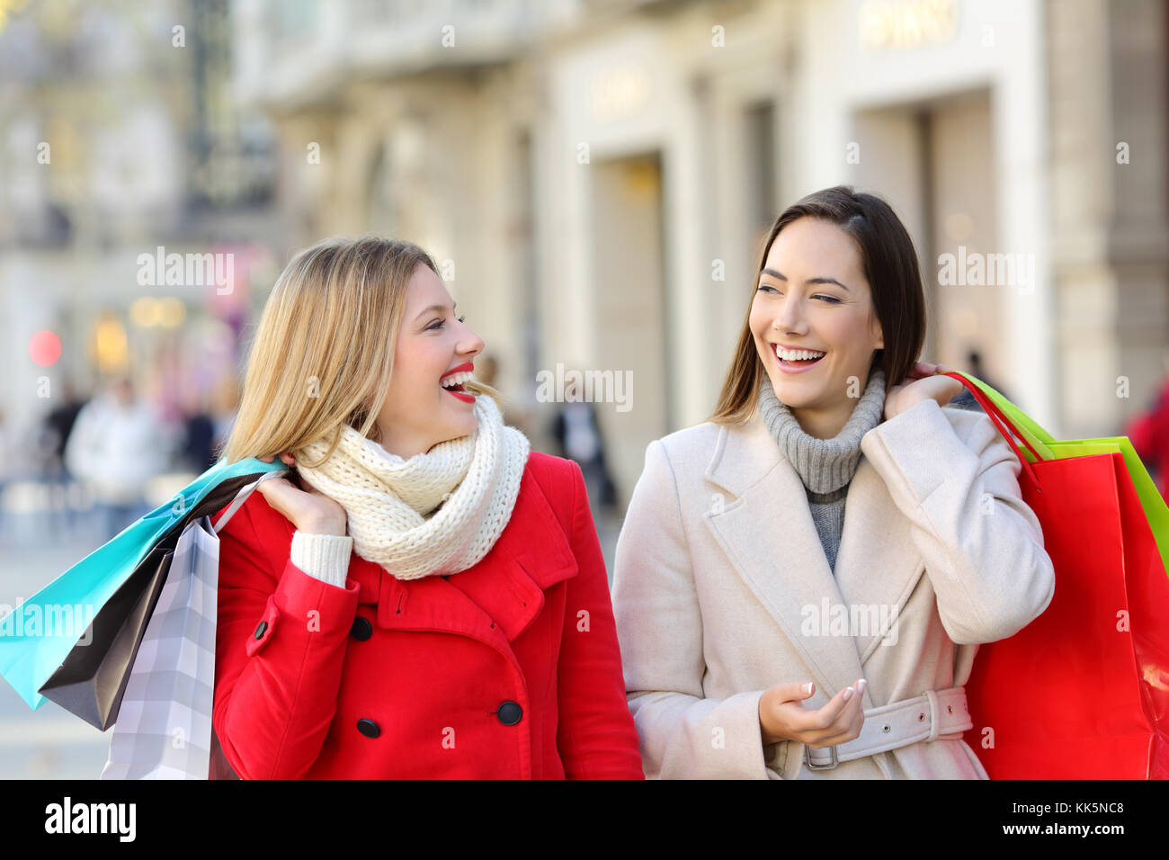 Two happy shoppers talking and walking on the street in winter Stock Photo